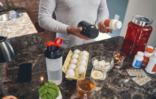 male holding two supplements in his hand with other health foods on the table like nuts and eggs