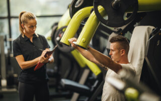 young male performing a chest exercise on a machine while his personal trainer records his efforts