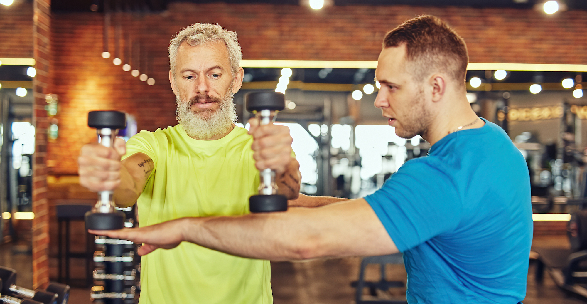 personal trainer in gym is assisting his client with a dumbbell lateral rais