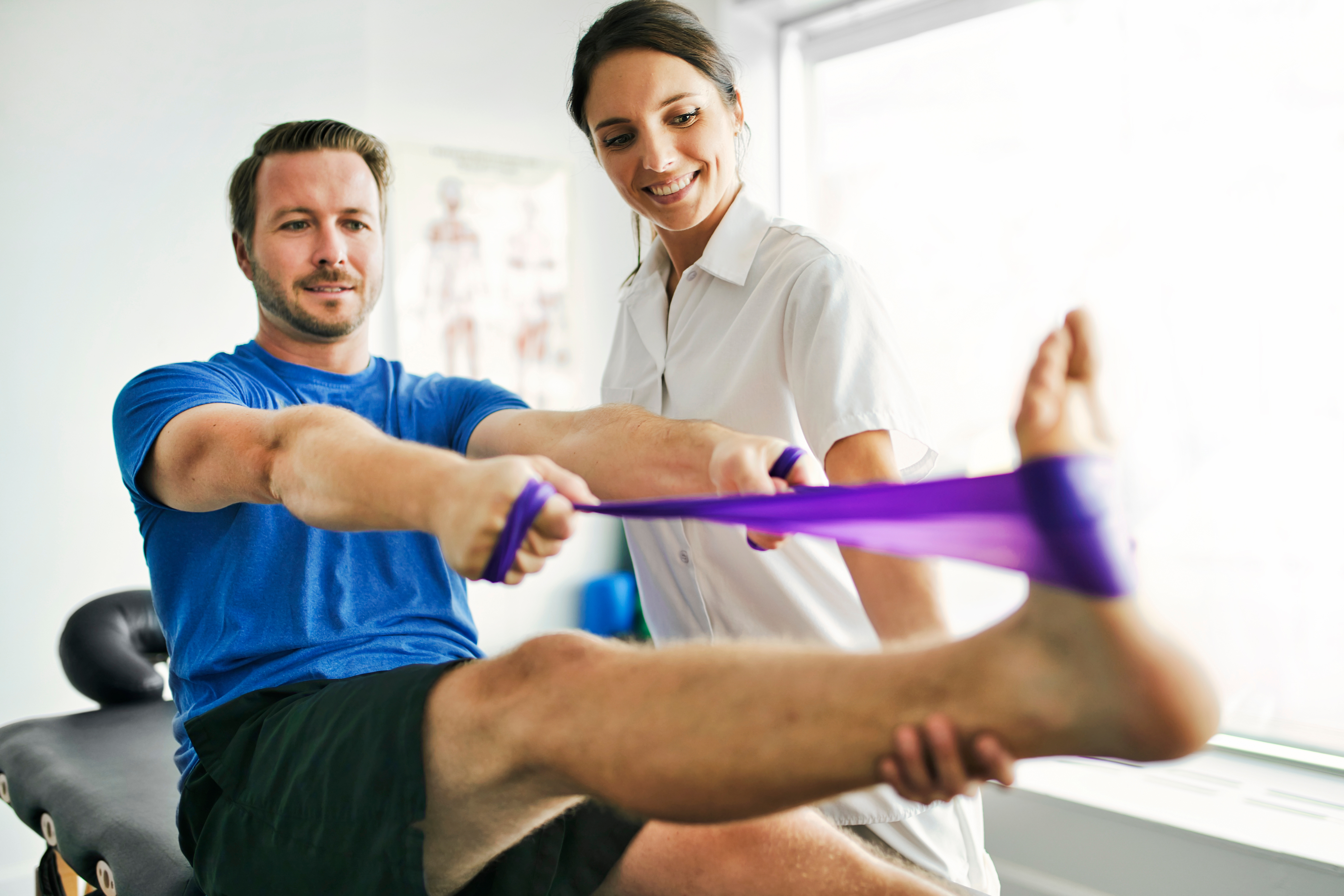 male patient performing a rehabilitation movement with a resistance band while female therapist assists him