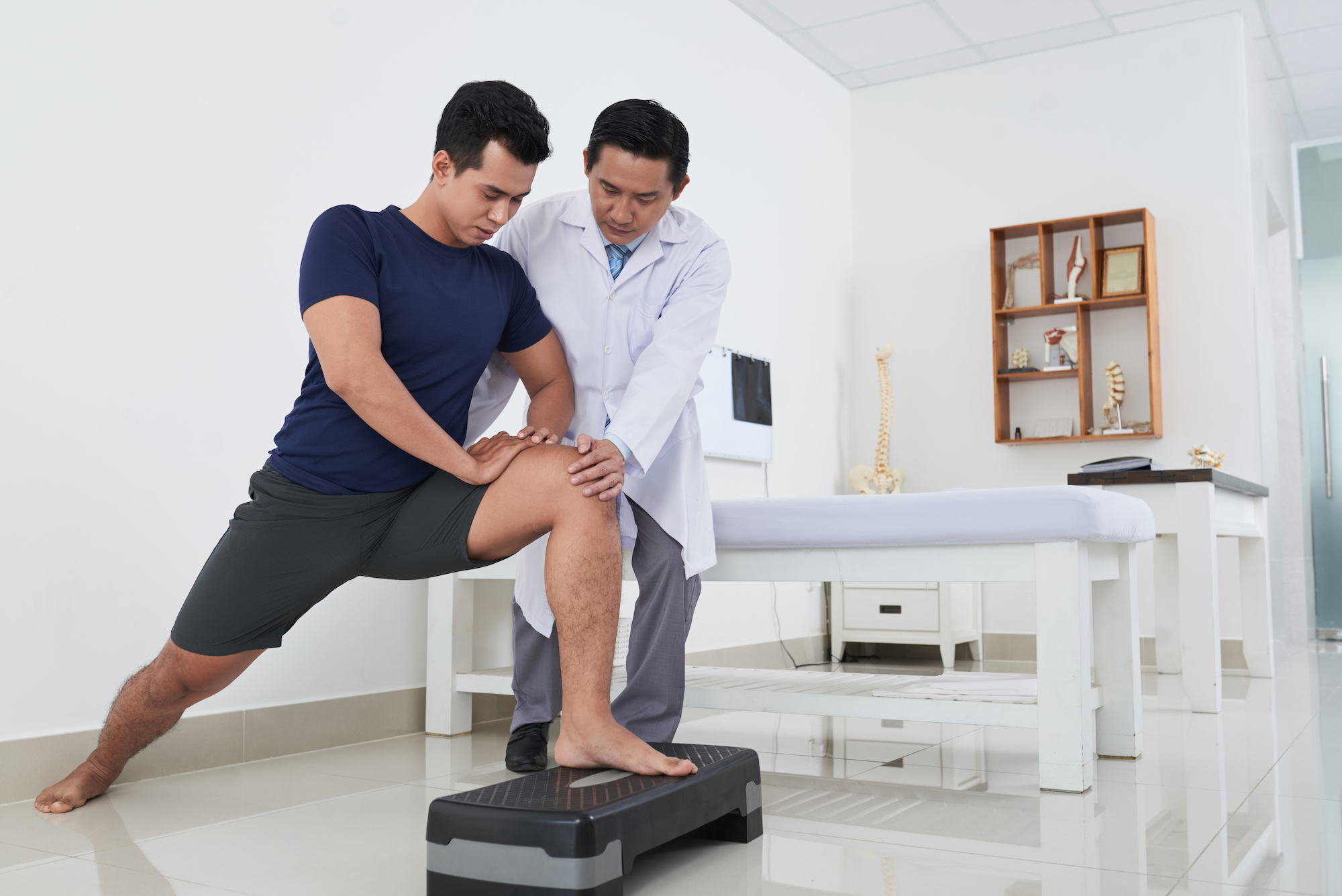 male doctor helping young male patient with a rehabilitation movement