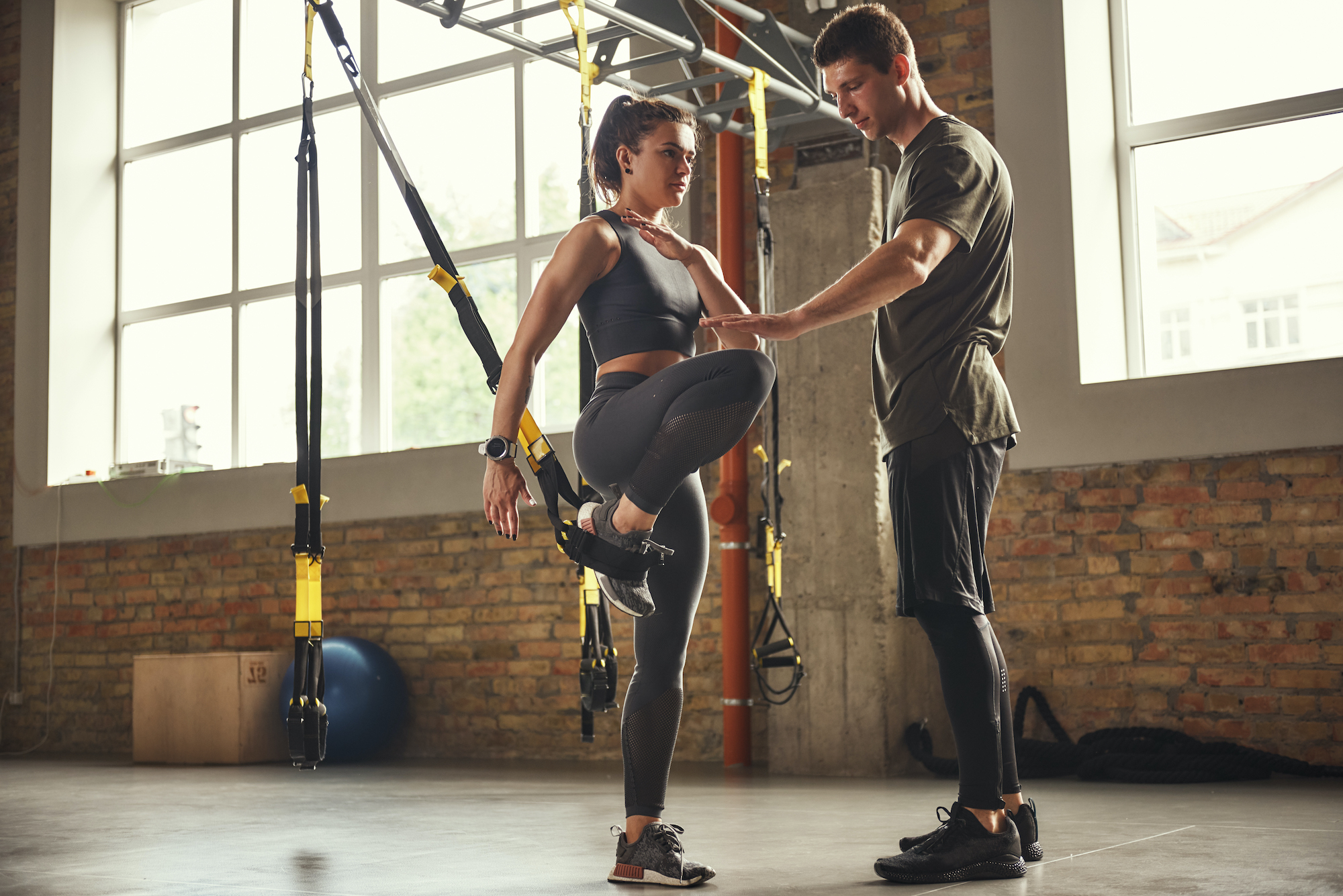 male personal trainer guiding female client through TRX movements.