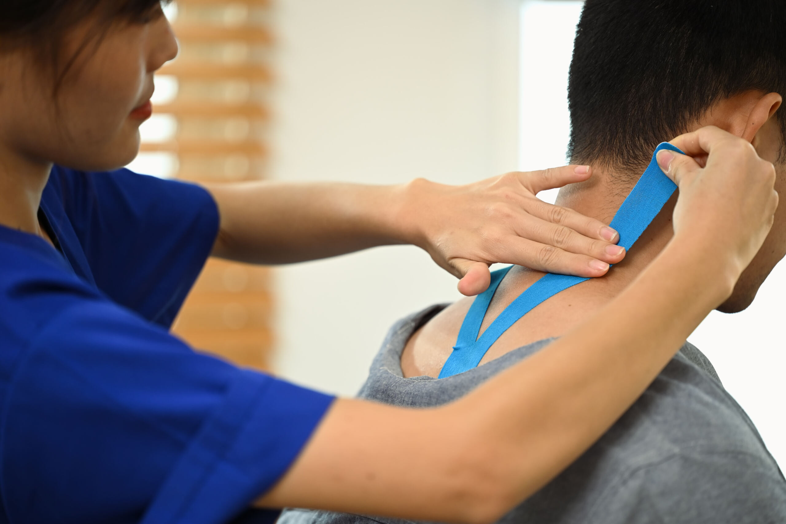 Female physiotherapist applying kinesiology tape on neck of injured male athlete. Sport physical therapy