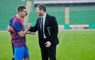 A sports manager or coach shaking hands with a soccer player on the field, representing professional careers in the sports industry.
