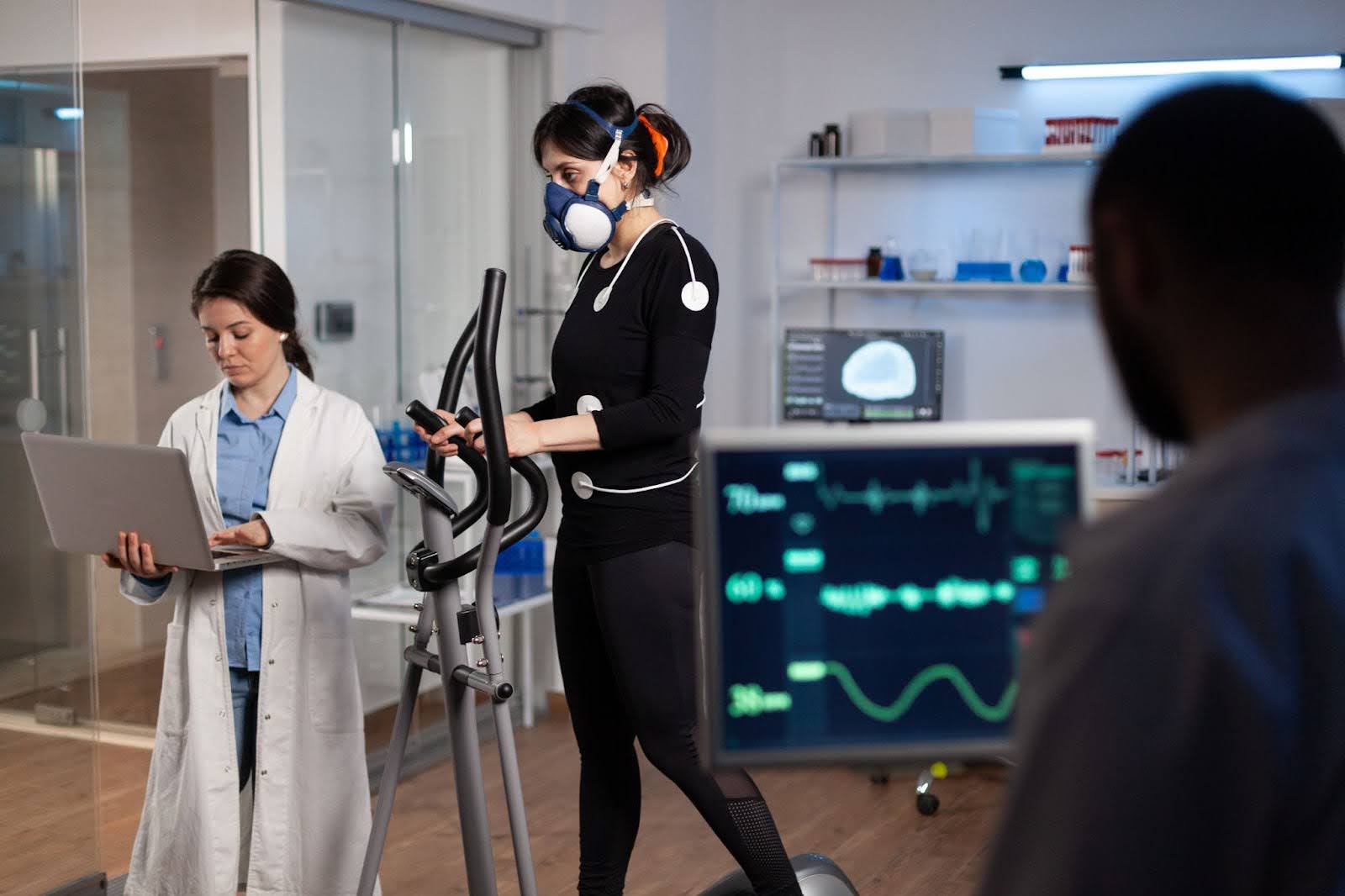 A strength and conditioning coach monitoring an athlete’s performance using advanced lab equipment during a treadmill exercise