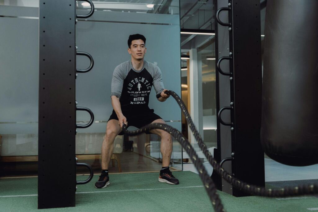Man performing battle rope exercise as part of tactical strength training in a modern gym.