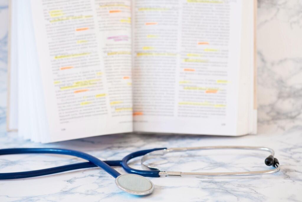Stethoscope placed beside an open medical textbook with highlighted terms, representing kinesiology or medical terminology study