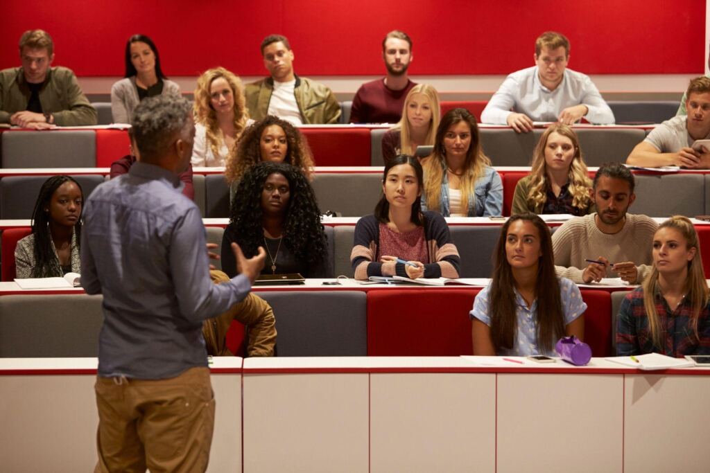 College students attentively listening to a professor in a lecture hall, possibly during a kinesiology or health sciences class
