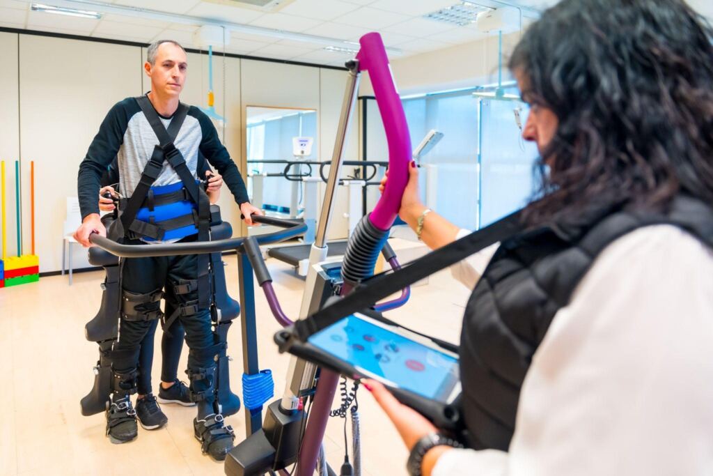 Physical therapist assisting a patient with robotic exoskeleton gait training during a rehabilitation session in a clinical setting