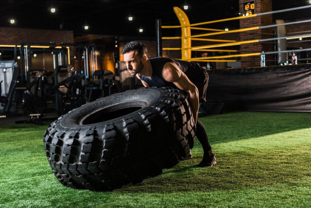 Man performing tactical strength training by flipping a heavy tire in a gym environment.